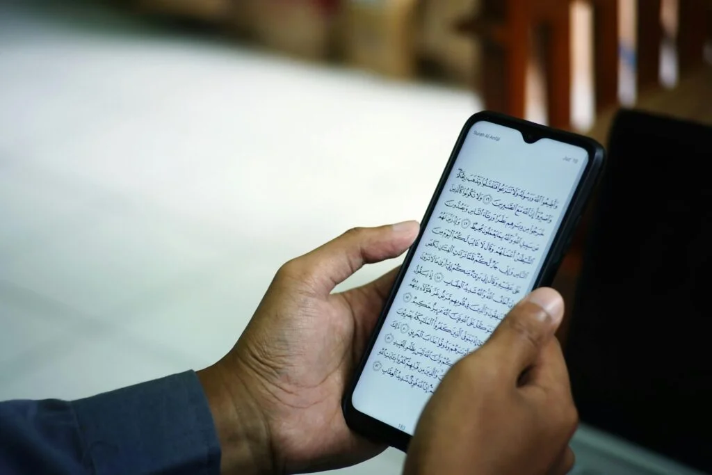 A man reading the Quran on a smartphone inside a mosque, symbolizing modern technology meeting traditional faith.